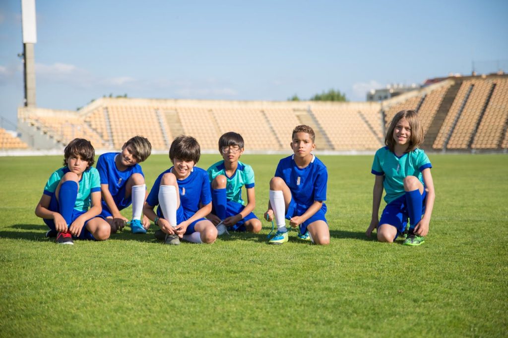 Youth soccer players sitting on a field, ready for training on a sunny day.