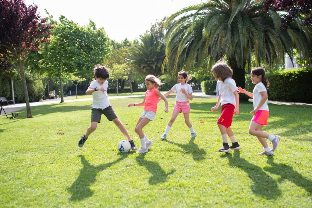 Group of kids enjoying a game of soccer in a lush green park on a sunny day in Portugal.